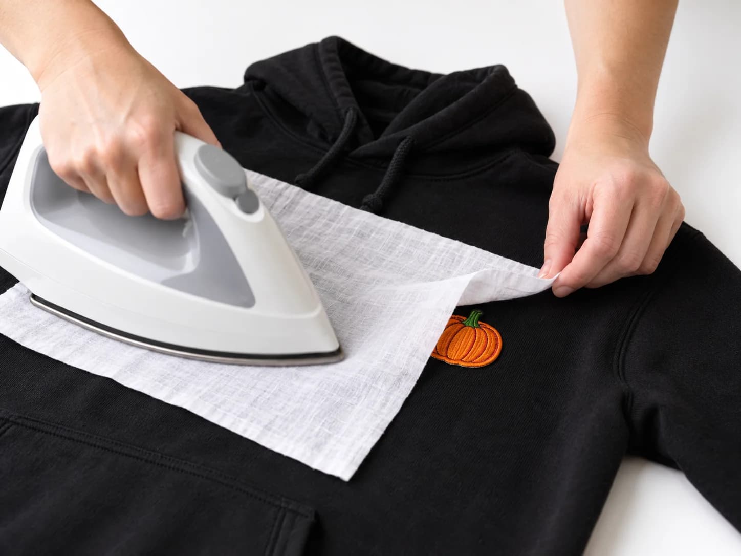 Hands ironing an embroidered pumpkin patch onto a black hoodie